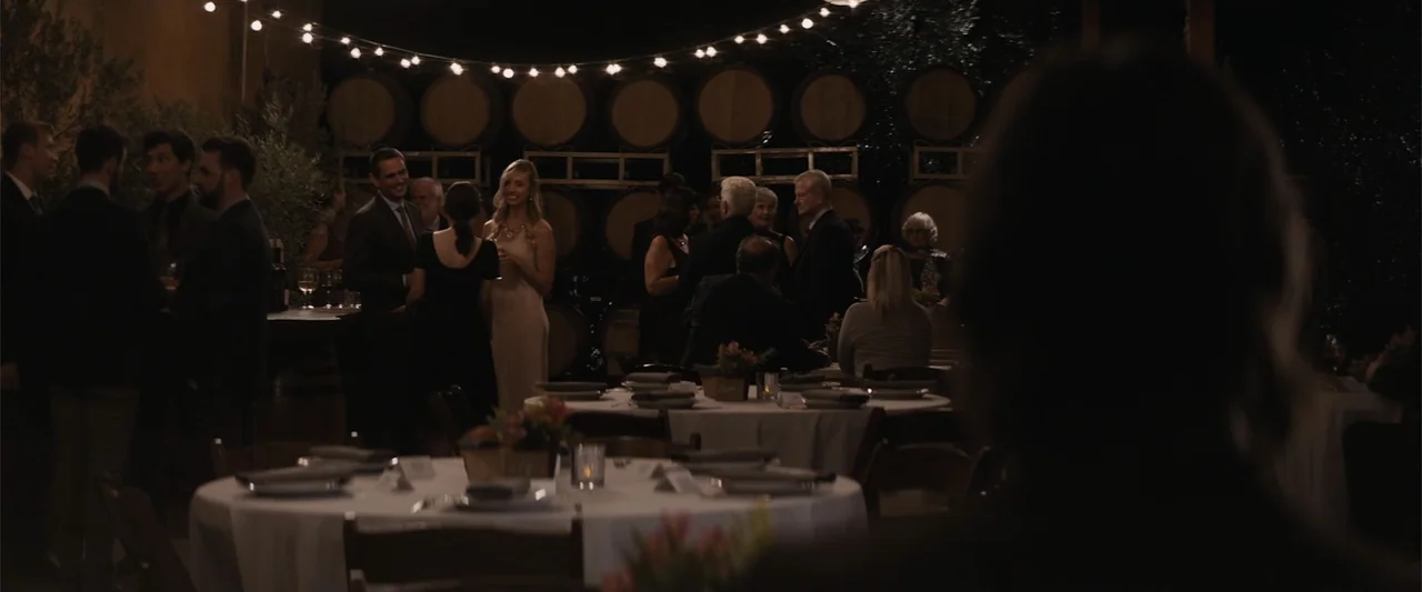 Destination Wedding (2018) movie still: wide — An outdoor winery space features round dining tables and rows of barrels in the background. A group…