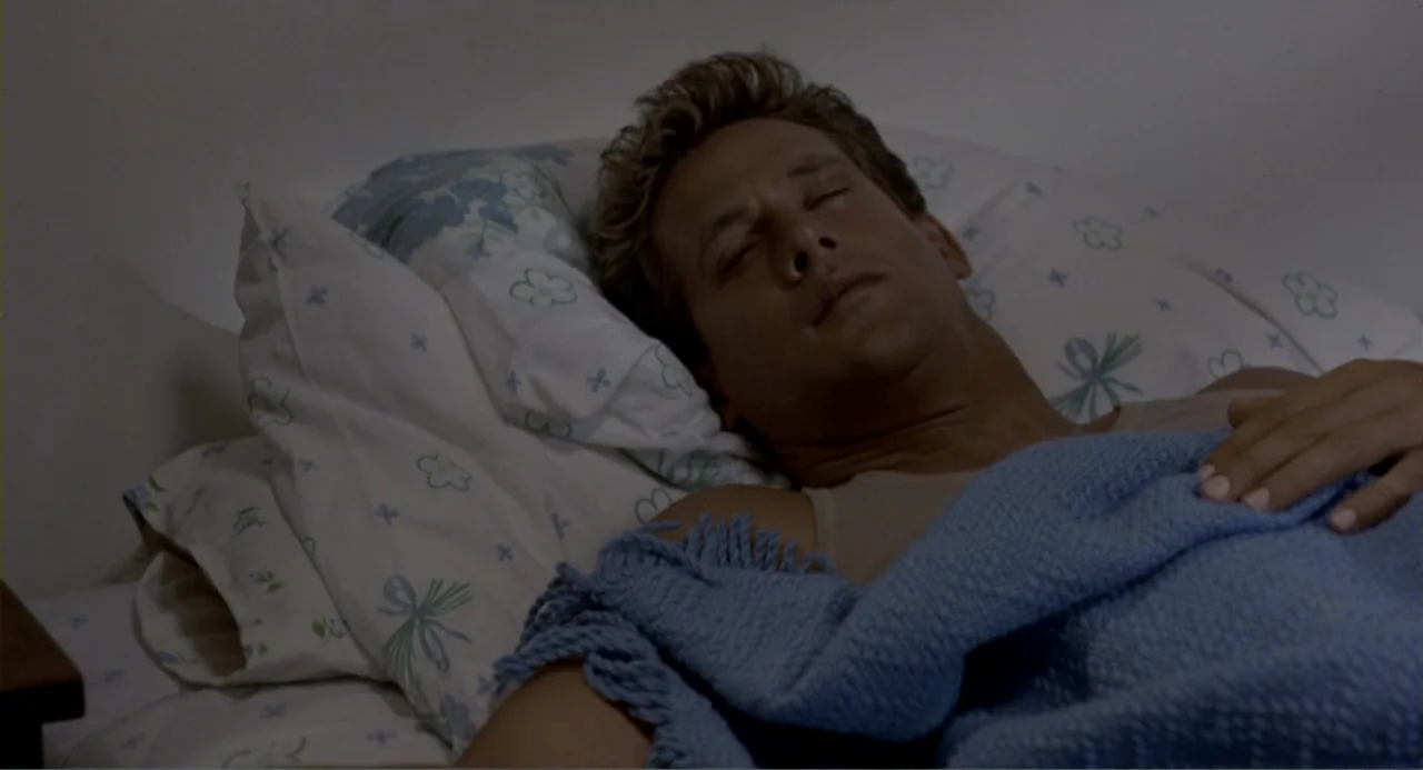 American Ninja 2: The Confrontation (1987) movie still: medium — A man lies asleep on a pillow with a patterned white and blue cover. He is covered…