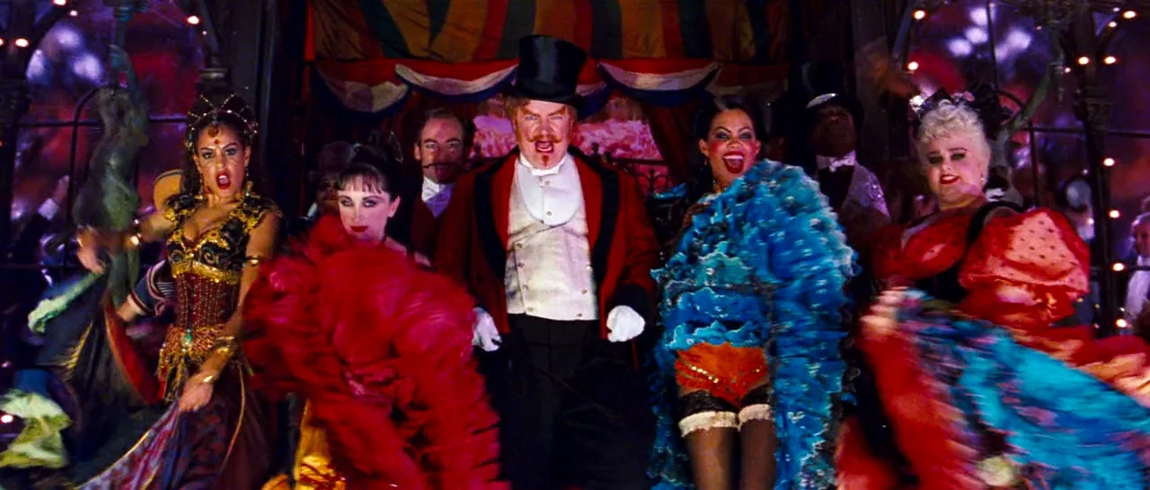 Moulin Rouge! (2001) movie still: fullbody — A theatrical stage with red curtains and string lights overhead provides the backdrop. A ringmaster in…