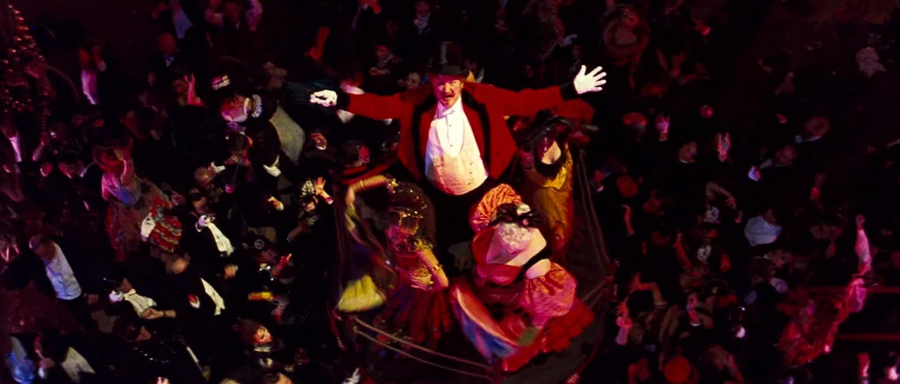 Moulin Rouge! (2001) movie still: An intense, high-angle wide shot captures a flamboyant ringmaster at the center of a swirling, dense masquerade…