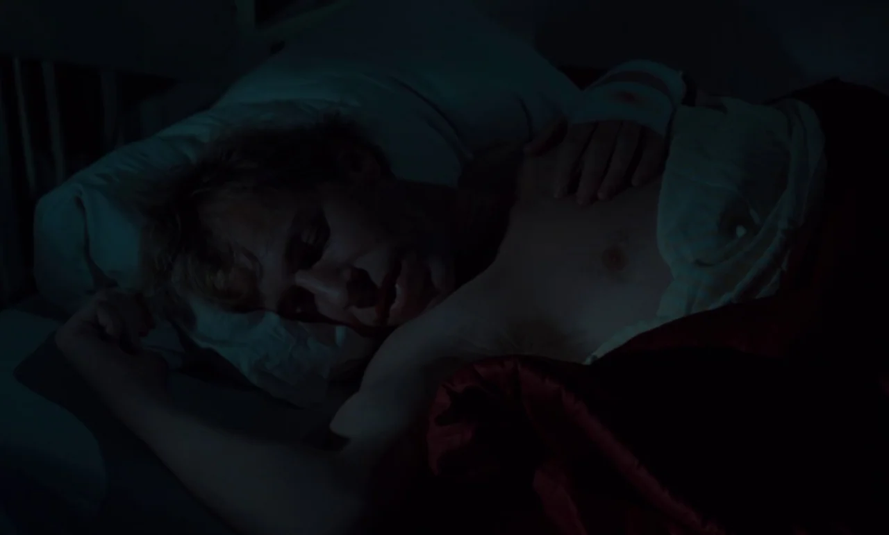 Wrong Move (1975) movie still: closeup — A dark bedroom with white bedding and a single person resting. The man lies under a dark red blanket with…