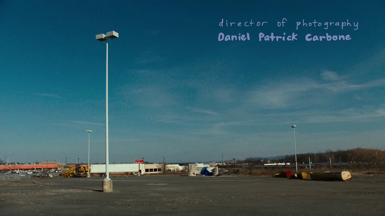 We’re All Going to the World’s Fair (2021) movie still: establishing — An expansive asphalt parking lot features multiple light poles and scattered…