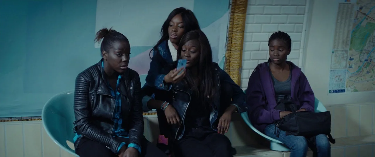 Girlhood (2014) movie still: medium — A public transport transit area with cream-colored subway tiles on the curved walls. Three young women sit on…