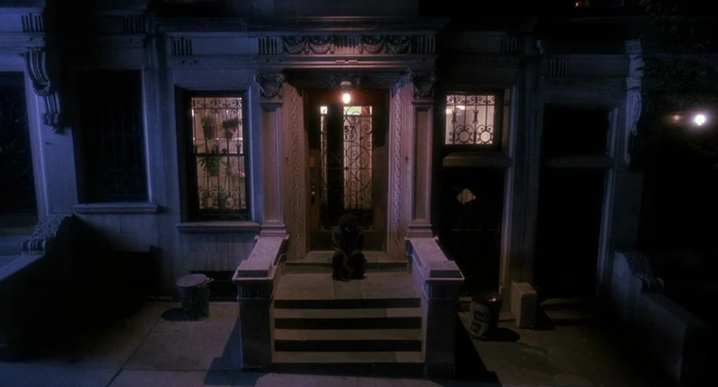 Mo’ Better Blues (1990) movie still: wide — A classic city brownstone features an ornate stone stoop and metal security gate. A lone figure sits in…