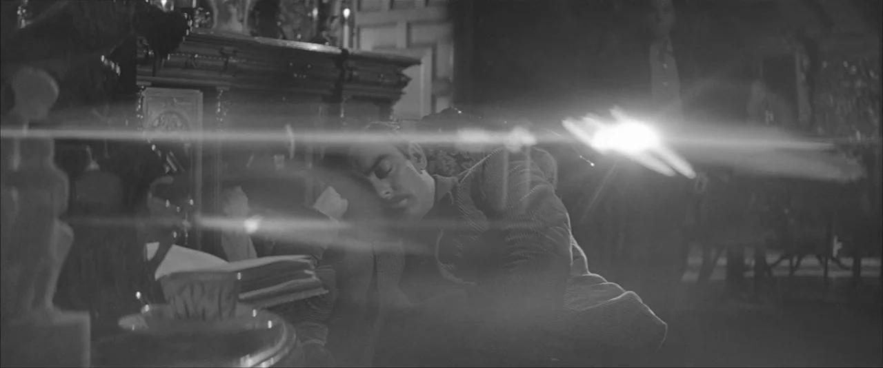 The Haunting (1963) movie still: medium — A dimly lit room features a man slumped in an ornate armchair. A sharp, horizontal light flare cuts across…