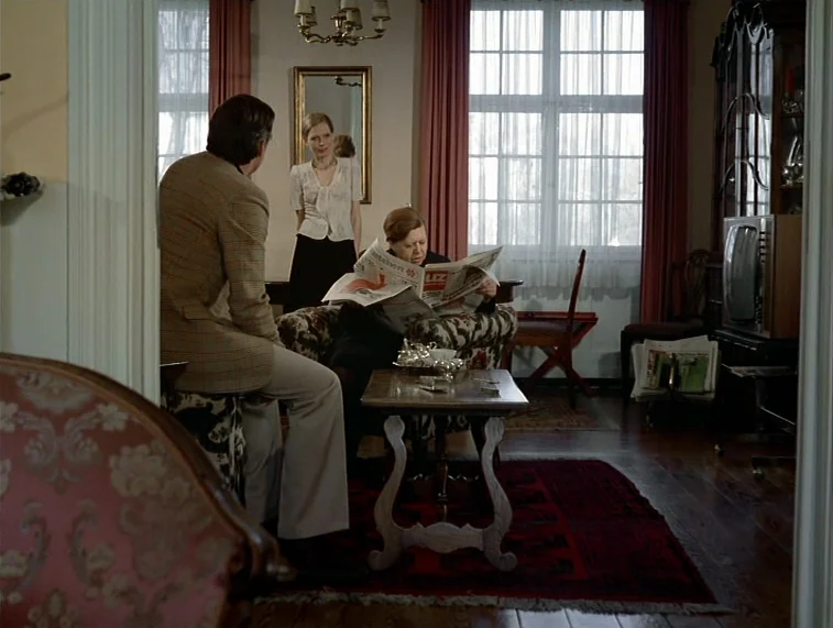 Mother Kusters Goes To Heaven (1975) movie still: medium — A well-lit interior room with patterned upholstery and a wooden coffee table. A man and…