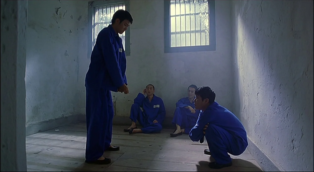 3-Iron (2004) movie still: fullbody — A stark room with off-white plaster walls and a wooden floor has barred windows. Four men wearing matching…