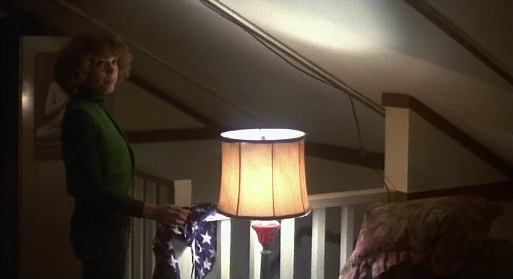 Coming Home (1978) movie still: medium — A dimly lit attic space features a low sloped ceiling and white wooden railings. A woman stands beside a…