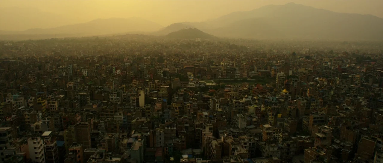 Doctor Strange (2016) movie still: establishing — A dense urban sprawl stretches toward low-lying mountains under a golden hazy sky. Countless…