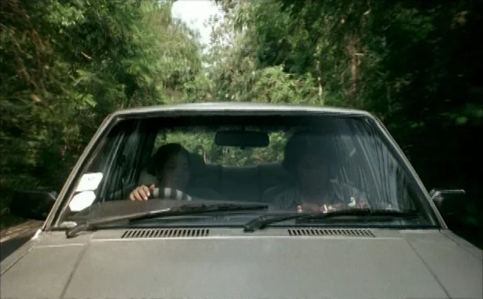 Blissfully Yours (2002) movie still: medium — A car moves along a narrow road surrounded by dense, lush green trees. Two individuals are inside the…