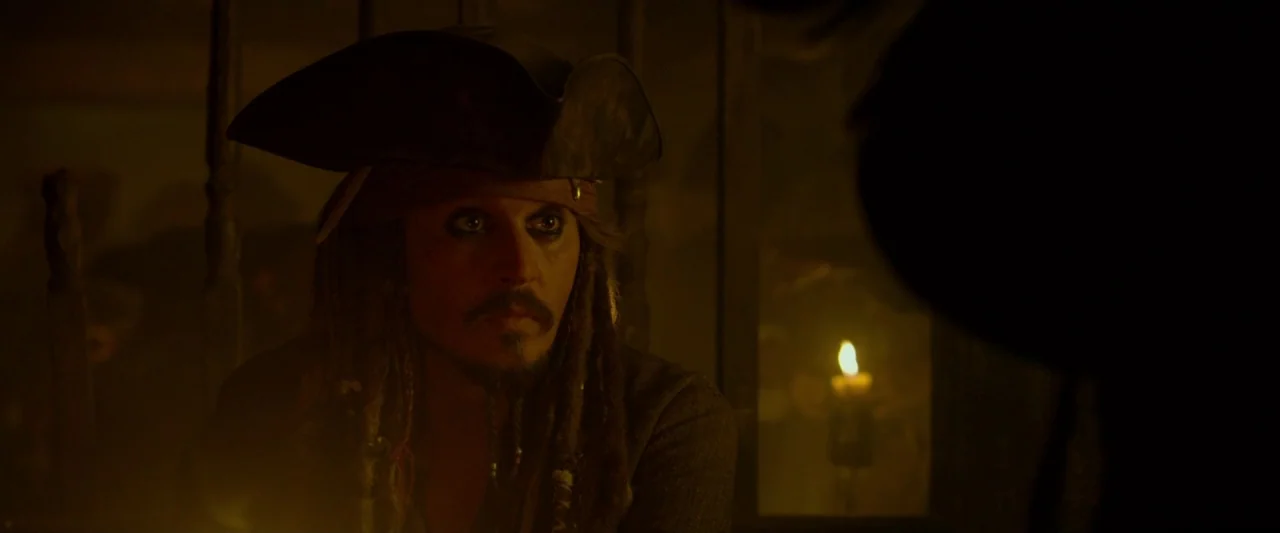 Pirates of the Caribbean: On Stranger Tides movie still: medium — A dimly lit room with wooden walls and shadows. A man in a tricorn hat sits in low…