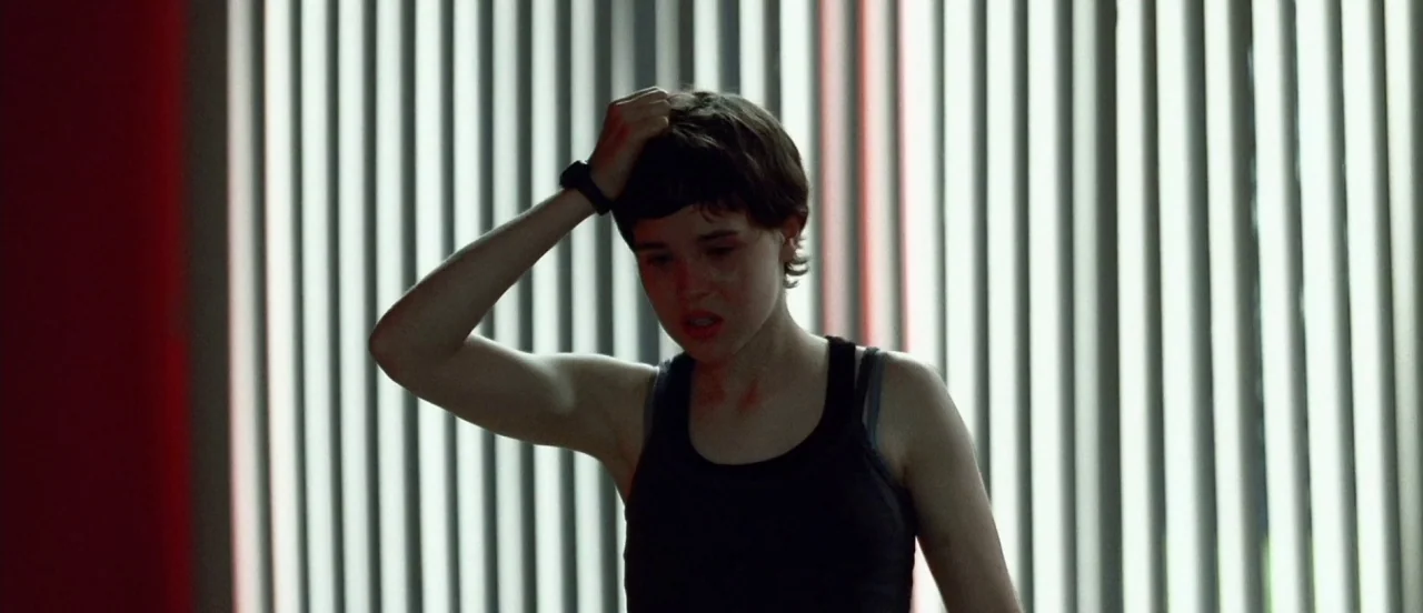 Hard Candy (2005) movie still: medium — A person stands before a window covered by closed vertical blinds. The individual looks downward with a hand…