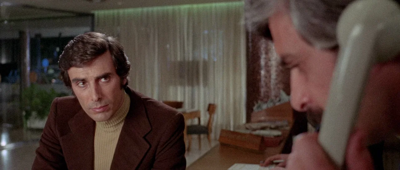 The Case of the Scorpion’s Tail (1971) movie still: medium — A dimly lit room with thin white curtains and wooden furniture. A man holds a telephone…