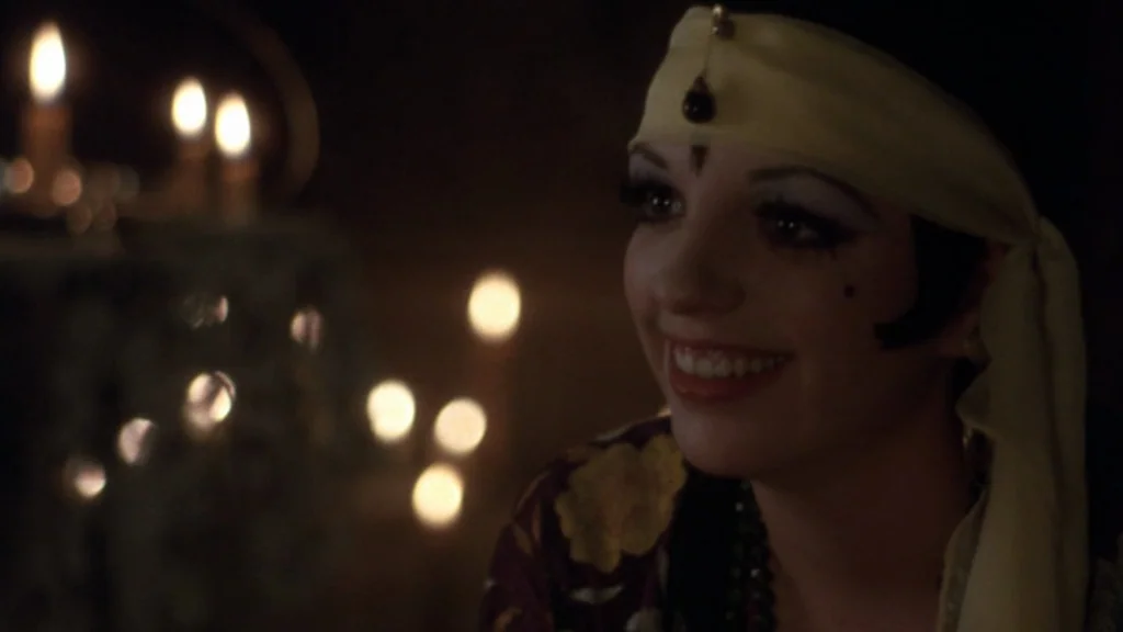 Cabaret (1972) movie still: closeup — A dark, dimly lit environment features soft candle flickers in the background. A young woman with heavy makeup…