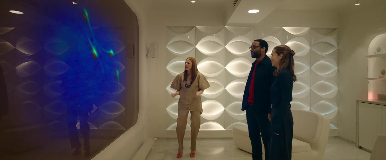The Pod Generation (2023) movie still: medium — A modern, sterile room features white paneled walls with repeated oval geometric light fixtures.…
