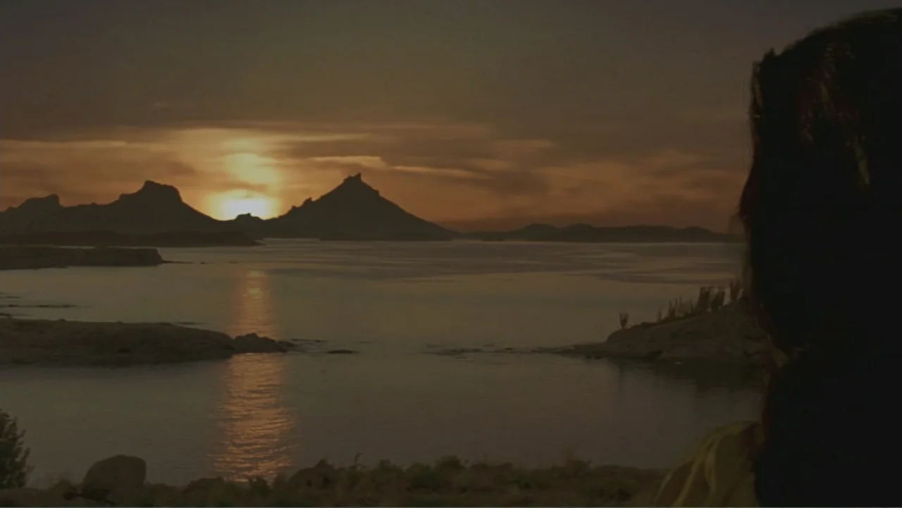 The Mask of Zorro (1998) movie still: medium — A dark mountainous landscape overlooks a wide body of water during sunset. A person stands on the…