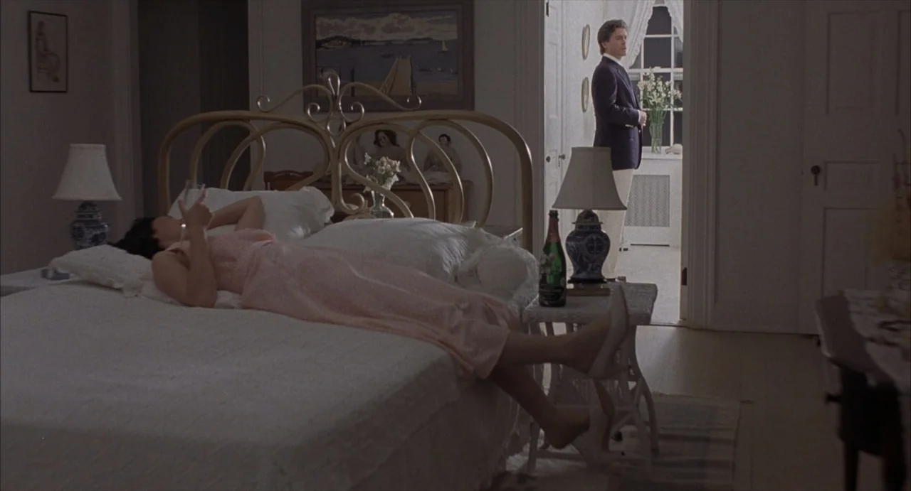 Masquerade (2023) movie still: wide — A well-lit bedroom features a large iron-framed bed and traditional furniture. A woman rests on the bed while…