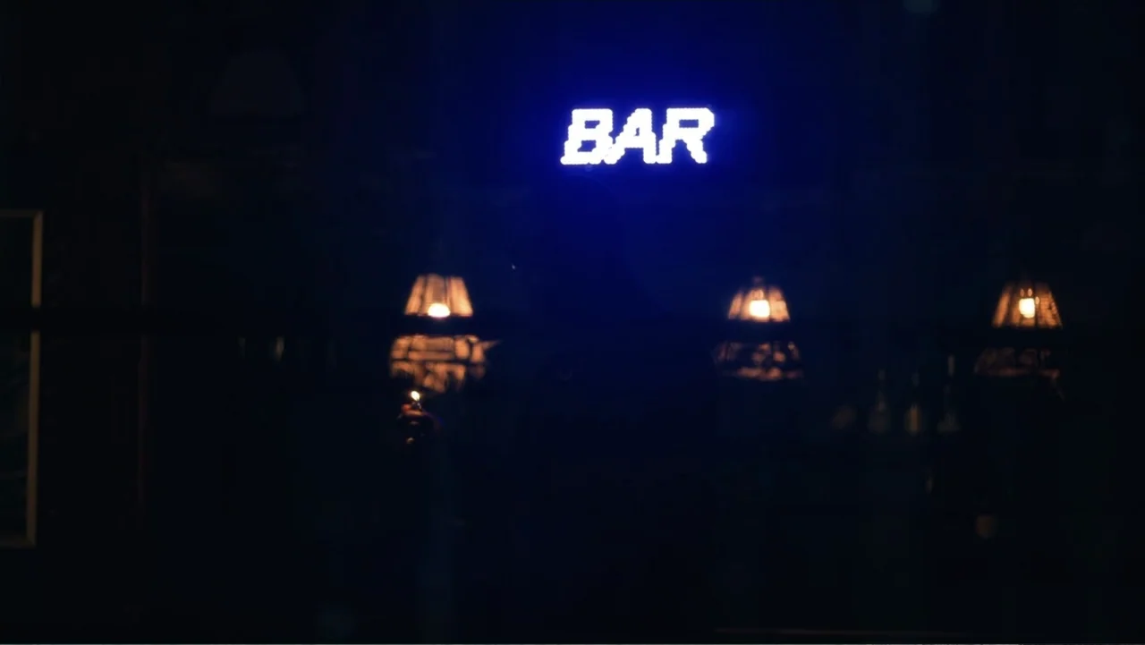 SIN: Blackout (2025) movie still: medium — A dark, dimly lit lounge space features a prominent blue glowing neon bar sign. A silhouetted figure…