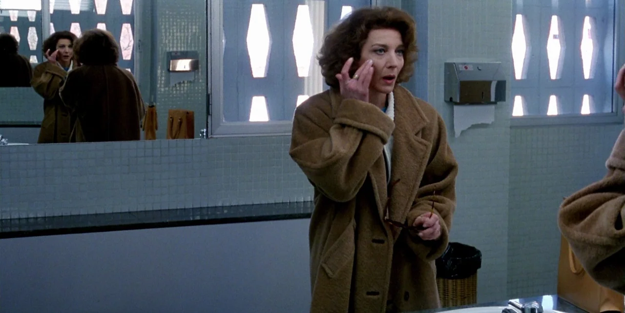 The Flower of My Secret (1995) movie still: medium — A public restroom with light blue wall tiles and distinctive geometric window panels. A woman…