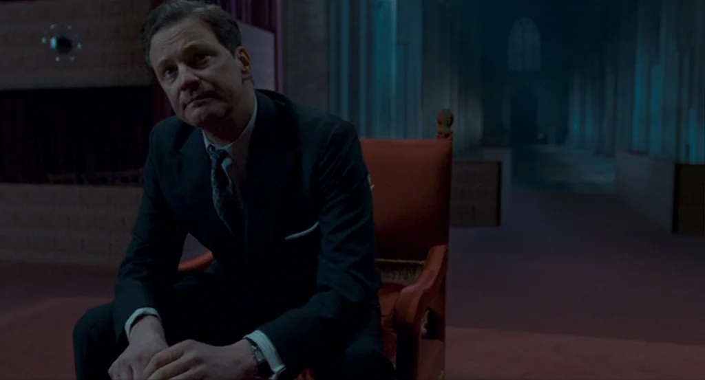 The King’s Speech (2010) movie still: medium — A spacious and dimly lit cathedral interior features dark columns and red carpeted floors. A man in a…