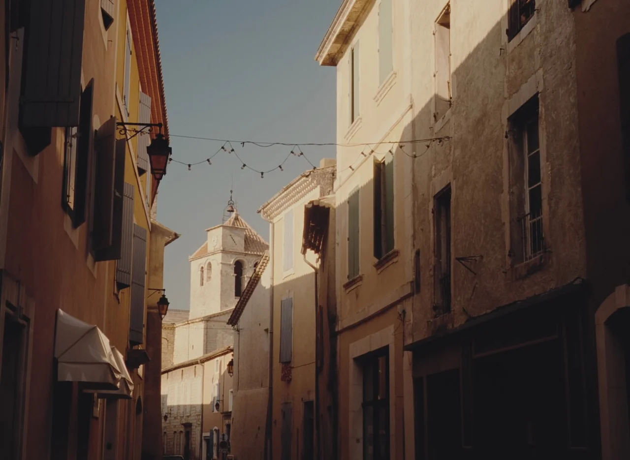 Autumn Tale (1998) movie still: establishing — A narrow Mediterranean street features tall yellow buildings with shutters and string lights…