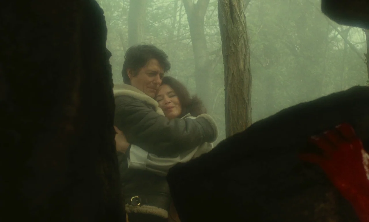 Litan (1982) movie still: medium — A man and woman embrace in a foggy, dense woodland area with tall trees. Large tree trunks frame the sides of the…