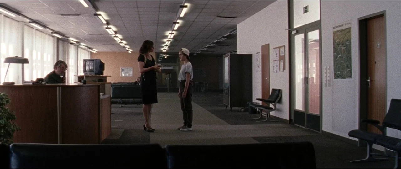 Luz (2018) movie still: fullbody — A spacious, sterile administrative lobby with carpeted floors, fluorescent ceiling lights, and modern furniture.…
