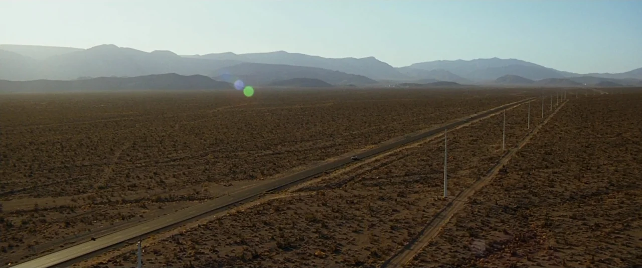 The Hangover (2009) movie still: establishing — A vast arid desert landscape stretches toward distant mountains under a clear sky. A long, straight…