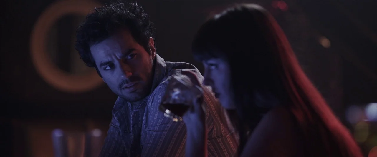 American Mary (2012) movie still: medium — A dimly lit bar interior features two people in conversation near the counter. The man watches the woman…