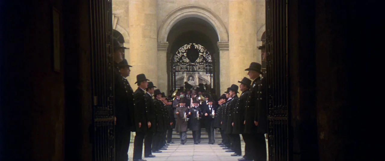 Heaven’s Gate (1980) movie still: wide — A stone courtyard with high arched doorways and ornate metal gates. A group of men in matching formal suits…