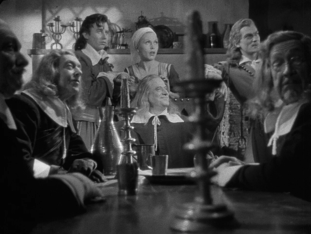 La Belle et la Bête (1946) movie still: medium — A dimly lit room with multiple figures seated around a long wooden dining table. The group looks…