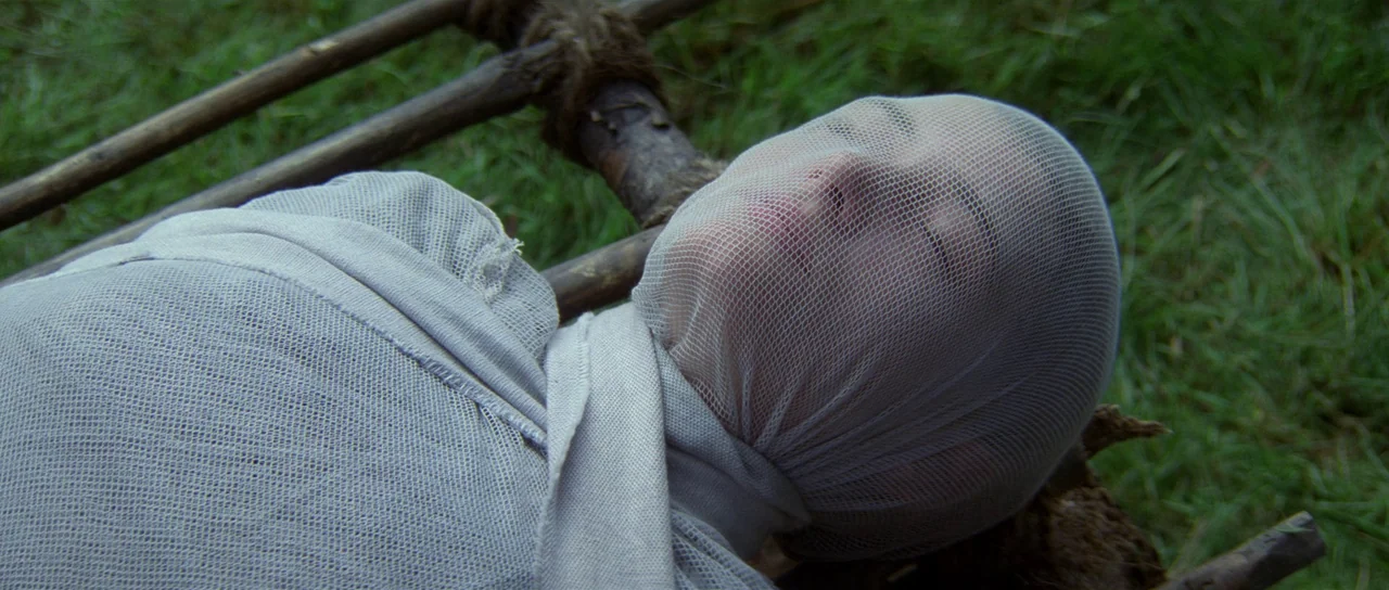 Braveheart (1995) movie still: closeup — A person lies on a wooden stretcher placed directly on green grass. The person is covered from the head…