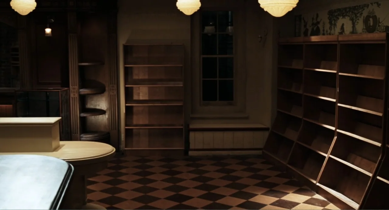 You've Got Mail (1998) movie still: establishing — An interior space features wooden shelving units against walls with a checkered floor pattern.…