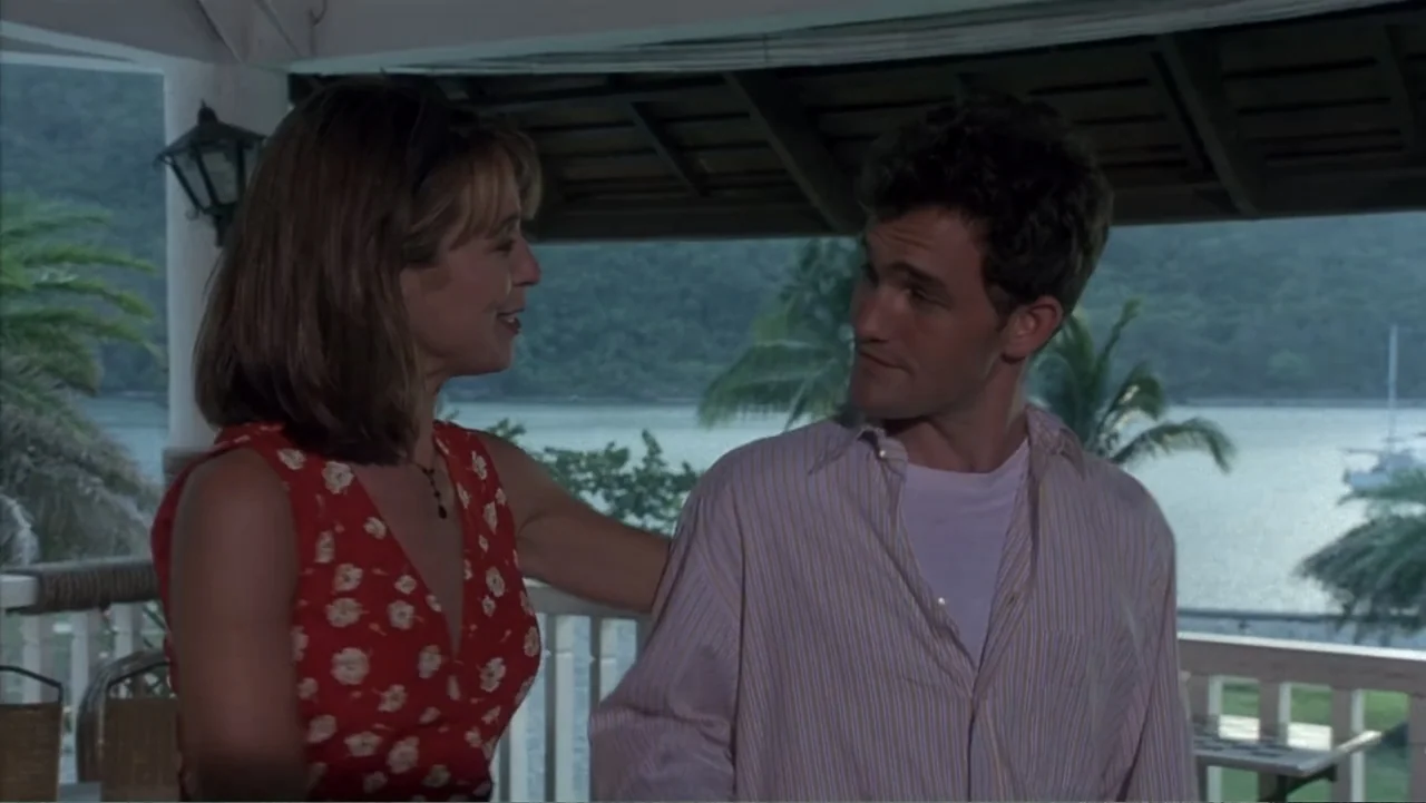 Behind Enemy Lines (2001) movie still: medium — A covered porch overlooks a tropical bay with palm trees and water in distance. A woman in a floral…