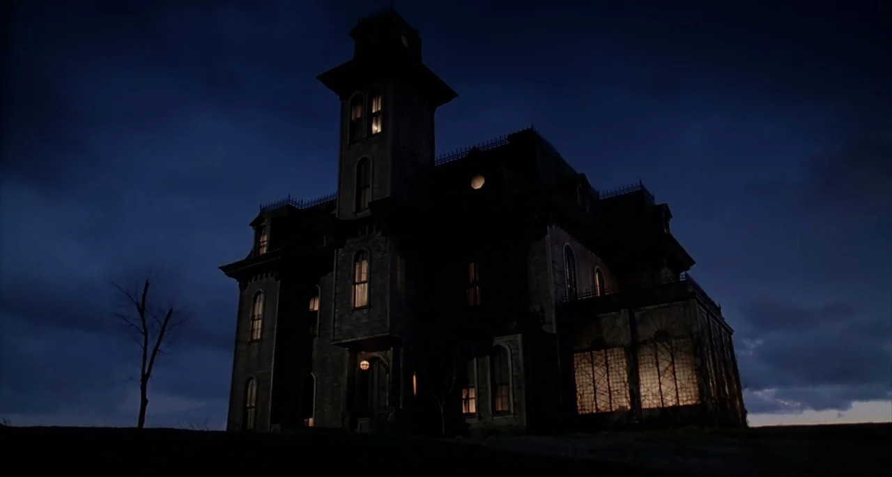 The Addams Family (1991) movie still: establishing — A dark Victorian-style mansion stands isolated on a grassy hill under a deep night sky. Warm…