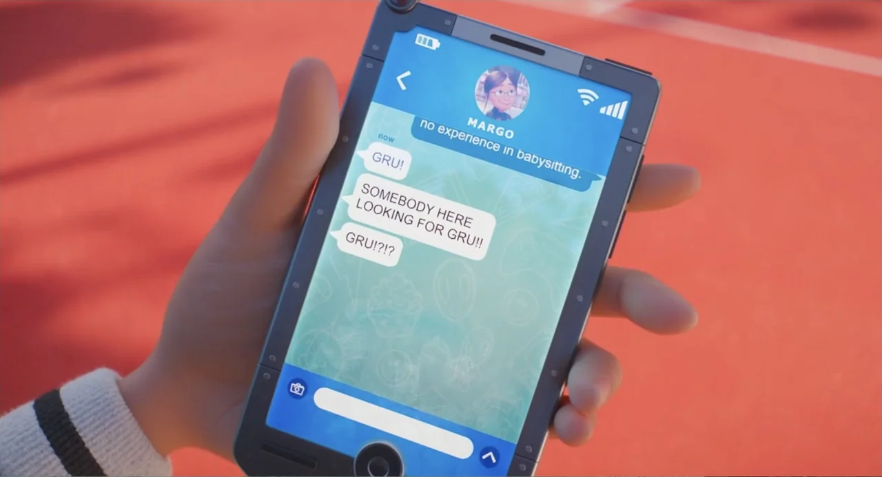 Despicable Me 4 (2024) movie still: closeup — A person's hand holds a smartphone against a red running track backdrop. The screen displays a chat…
