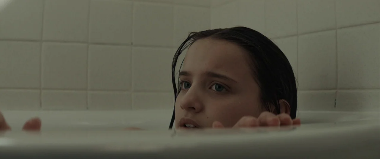 The Black Phone (2021) movie still: closeup — A close-up of a child inside a plain, white tiled bathtub. The subject rests hands on the tub rim…