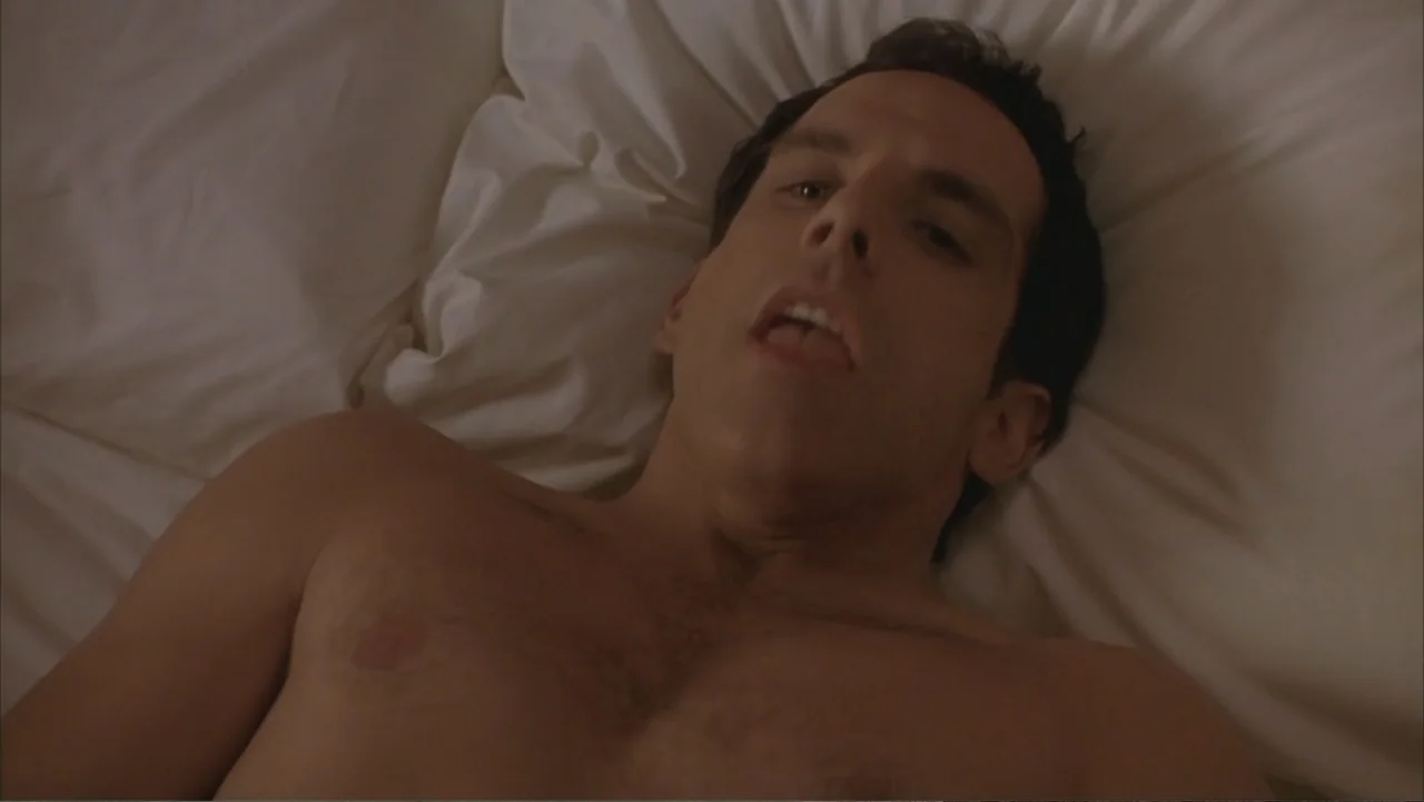 Along Came Polly (2004) movie still: closeup — A man lies on white bed linens in a brightly lit room. The subject reclines on his back with his…