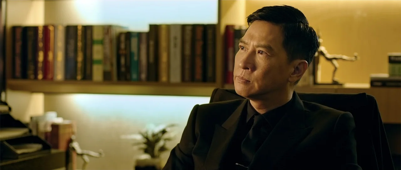 Line Walker (2016) movie still: medium — A man sits before shelves filled with books in a dimly lit office. The subject sits in a black chair while…