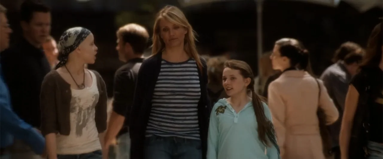 My Sister's Keeper (2023) movie still: medium — A public outdoor walkway populated by people walking in the background. Three women walk toward the…