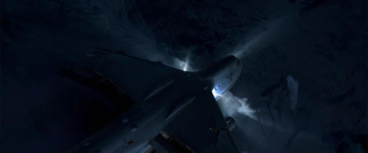 2012 (2009) movie still: wide — A passenger jet flies over a dark, snow-covered mountain range at night. Moonlight reflects off the plane's fuselage…