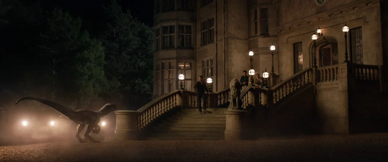 Jurassic World: Fallen Kingdom (2018) movie still: wide — A dark night outside a large stone mansion with an ornate staircase. A dinosaur stalks…