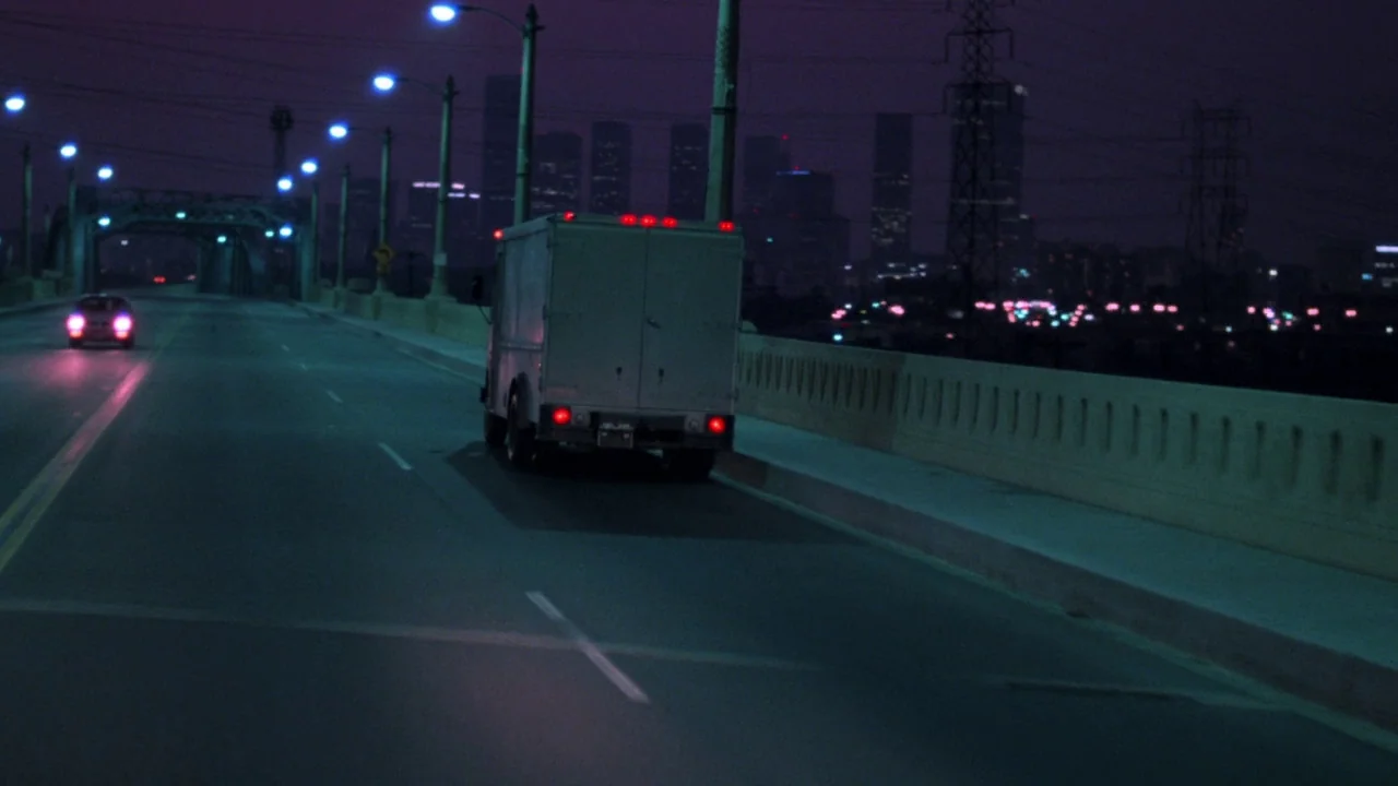 Repo Man (1984) movie still: wide — A city bridge at night features a white van driving toward the city skyline. Electric street lamps line the road…
