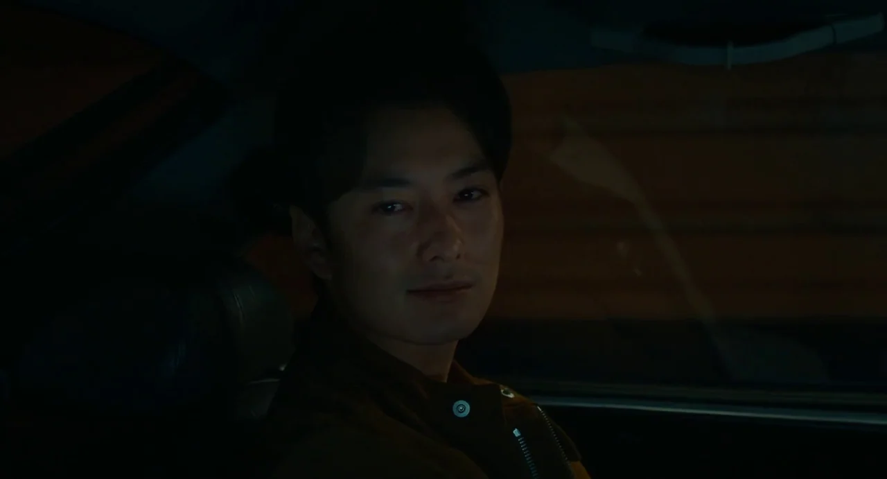 Drive My Car (2021) movie still: closeup — A man sits in the driver seat of a dark vehicle at night. Dim street lighting illuminates his face…