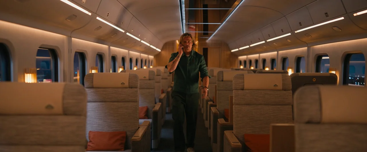 Bullet Train (2022) movie still: fullbody — A modern train car interior features rows of empty seats with tan upholstery. A man walks down the aisle…