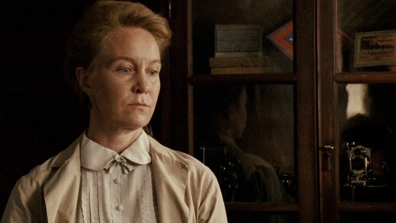 Everlasting Moments (2008) movie still: closeup — A woman stands indoors in front of a dark wooden cabinet with glass doors. The woman gazes to the…