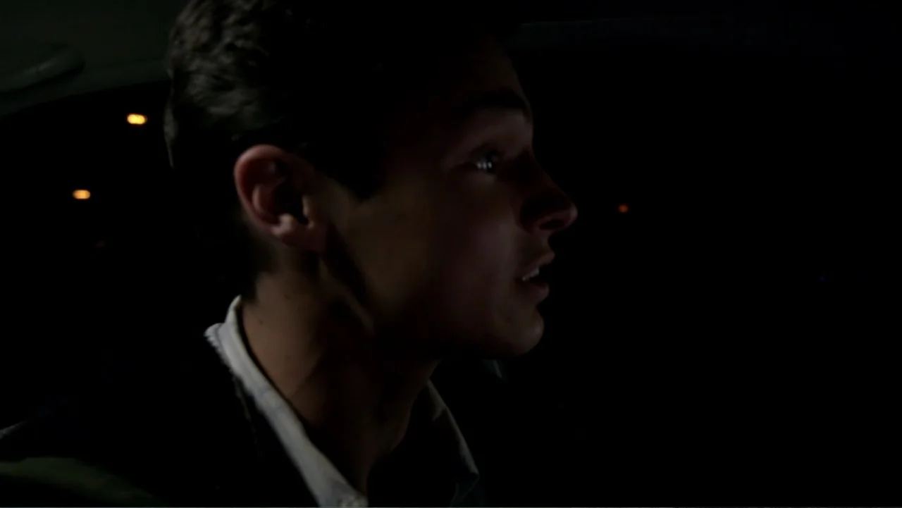 The Gallows (2015) movie still: closeup — A dark vehicle interior with the man illuminated by faint ambient light. The man looks ahead while sitting…