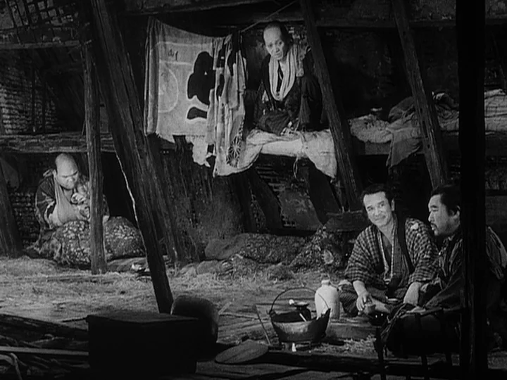 The Lower Depths (1957) movie still: wide — A dimly lit room with exposed wooden support beams and a packed dirt floor. Three men are gathered…