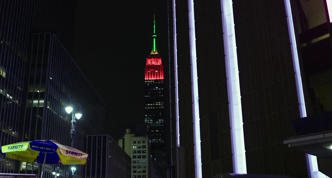 Last Flag Flying (2017) movie still: wide — A view of a New York City street at night with the Empire State Building visible. Bright white vertical…