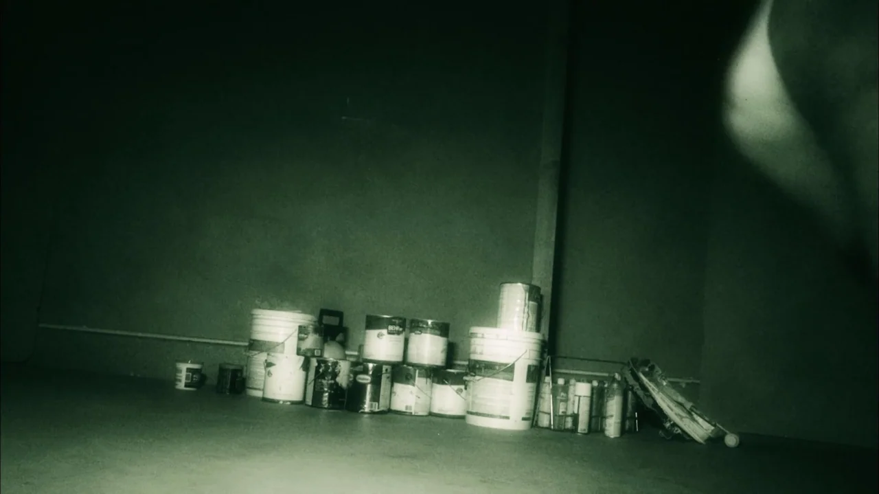 A Haunted House (2013) movie still: wide — A dark, spartan room contains a collection of paint cans lined against a wall. The objects are…